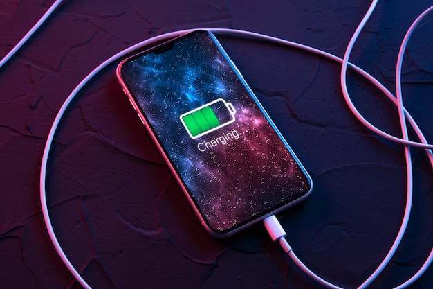 Téléphone intelligent mobile sur dispositif de chargement sans fil sur fond de couleur rouge et bleu néon foncé. Batterie de l'icône et éclairage de la progression de la charge sur l'écran.smartphones connectés à la source d'alimentation.Batterie faible