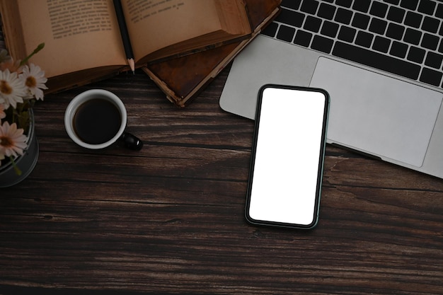 Téléphone intelligent avec une tasse de café d'ordinateur portable à écran blanc et un livre vintage sur une table en bois