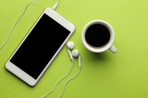 Téléphone intelligent. Téléphone et écouteurs blancs et une tasse de café sur un fond vert clair. vue de dessus.