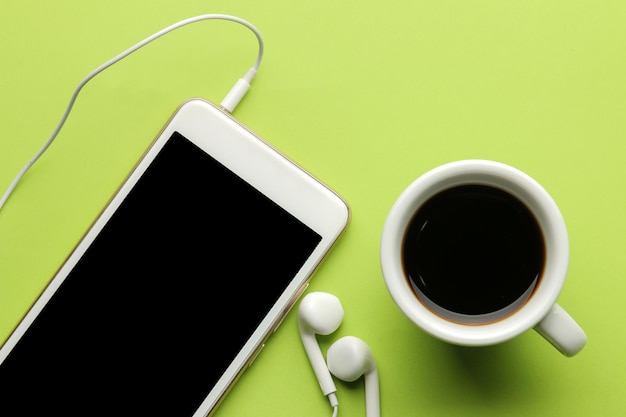 Téléphone intelligent. Téléphone et écouteurs blancs et une tasse de café sur un fond vert clair. vue de dessus.