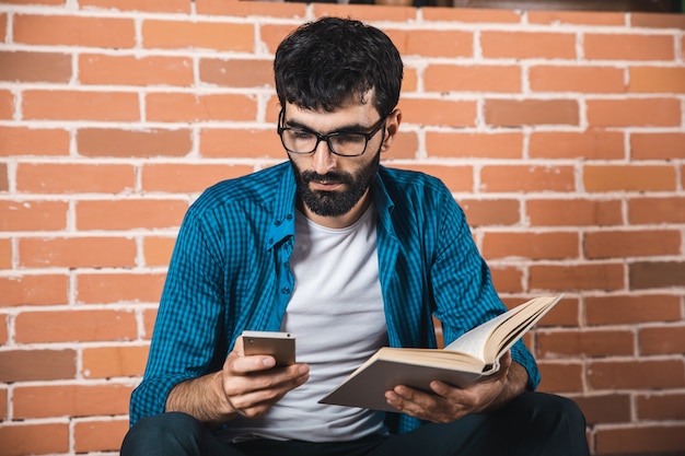 Téléphone main homme avec livre sur mur de briques