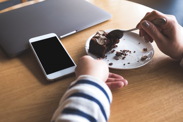 Téléphone mobile avec écran de bureau noir blanc à côté d'un ordinateur portable avec une femme mangeant un gâteau brownie