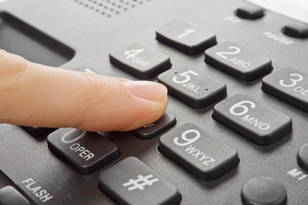 Téléphone noir de bureau avec la main d'isolement sur le blanc