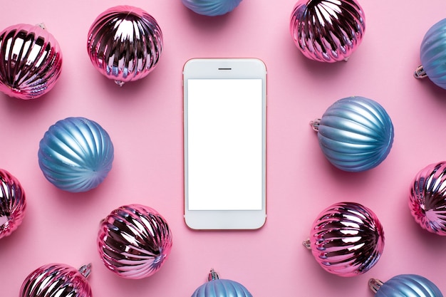 Téléphone portable et boules bleues et roses de Noël brillant pour la décoration sur fond rose, boule de nouvel an