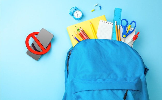 Téléphone portable dans le sac à dos Sac scolaire avec des fournitures pour l'école sur fond jaune Copier l'espace