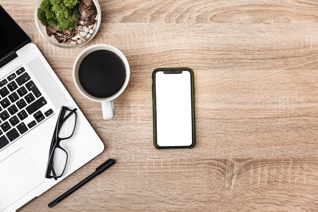 Un téléphone portable avec un écran blanc se trouve sur le bureau à côté d'un ordinateur portable, vue d'en haut