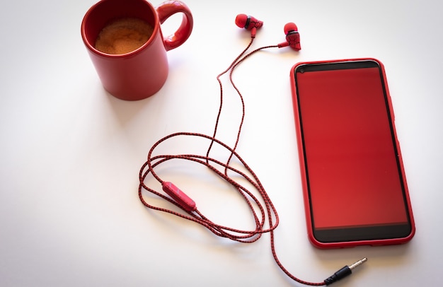 Téléphone portable avec écran rouge sur fond blanc, tasse à café rouge et écouteurs