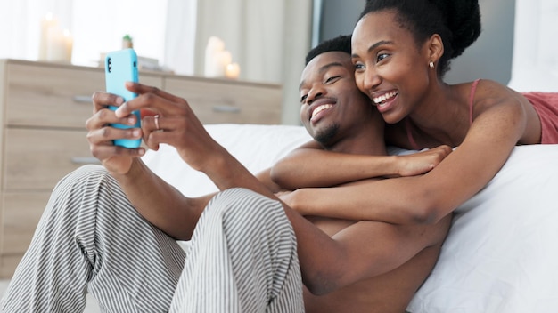 Le téléphone portrait et le couple prennent un selfie dans la chambre ensemble et le partagent sur l'application de réseau social en ligne le matin Le sourire des médias sociaux et la femme noire adore prendre des photos avec un partenaire africain