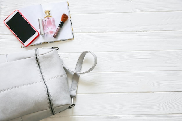 Téléphone, sac élégant et parfums sur fond blanc. Belle pose à plat. Choses pour femme d'affaires. Calendrier du carnet de notes. Kit de maquillage.