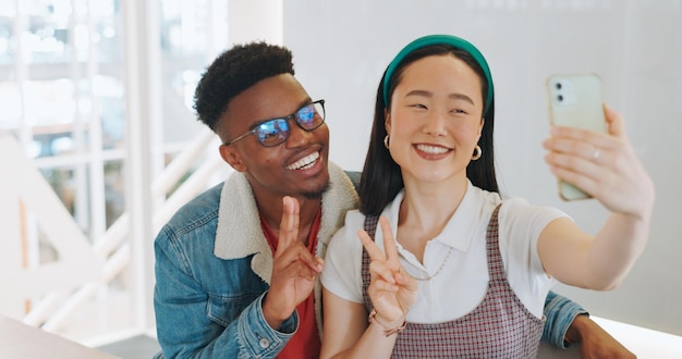 Photo téléphone selfie signe de paix et pouce levé d'un couple prenant des photos pour un souvenir heureux des médias sociaux ou d'un blog aimez la diversité et l'homme et la femme avec un geste de la main prenant une photo sur un smartphone à la maison