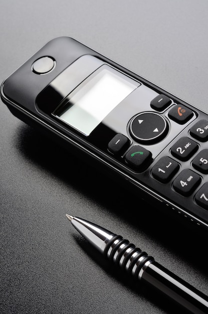 Le téléphone et le stylo à bille sont sur une surface grainée noire