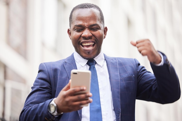 Téléphone à succès ou homme d'affaires heureux dans une ville pour célébrer la bonne nouvelle de la promotion de l'emploi ou des objectifs de vente Le gagnant ou l'homme noir excité célèbre la victoire d'un bonus ou d'un investissement financier réussi