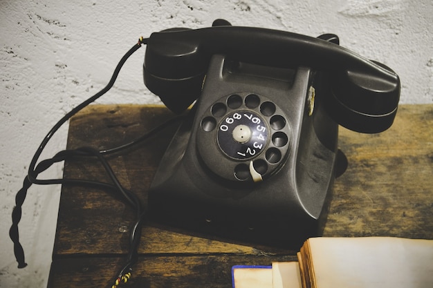 Téléphone vintage noir sur table en bois et mur de plâtre de ciment blanc grunge