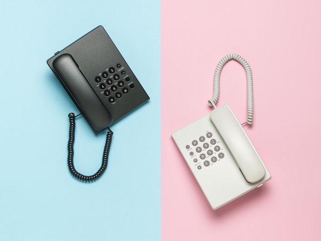 Téléphones rétro blancs et noirs sur fond rose et bleu Mise à plat