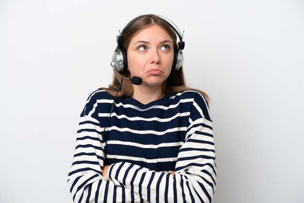 Télévendeur femme caucasienne travaillant avec un casque isolé sur fond blanc faisant des doutes geste tout en soulevant les épaules