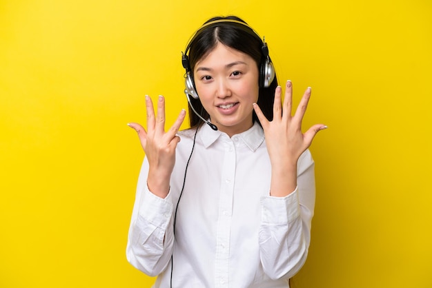 Télévendeur femme chinoise travaillant avec un casque isolé sur fond jaune comptant neuf avec les doigts