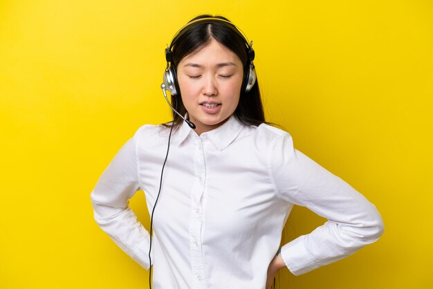 Télévendeur femme chinoise travaillant avec un casque isolé sur fond jaune souffrant de maux de dos pour avoir fait un effort