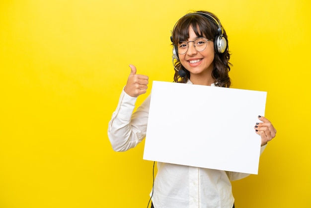 Télévendeur femme latine travaillant avec un casque isolé sur fond jaune tenant une pancarte vide et pointant du côté