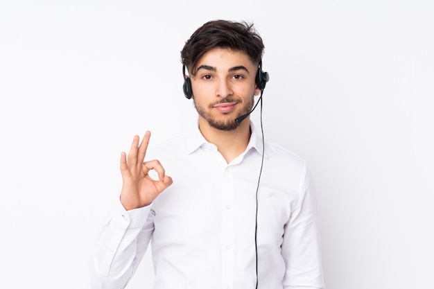 Télévendeur homme arabe travaillant avec un casque isolé sur mur blanc montrant un signe ok avec les doigts