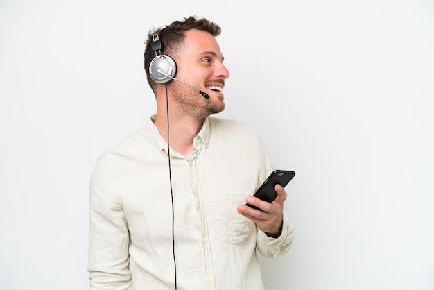 Télévendeur homme caucasien travaillant avec un casque isolé sur fond blanc en gardant une conversation avec le téléphone mobile avec quelqu'un