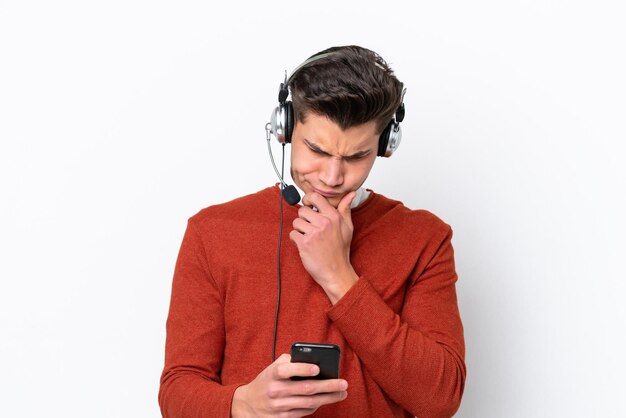 Télévendeur homme caucasien travaillant avec un casque isolé sur fond blanc pensant et envoyant un message