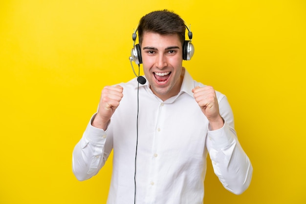 Télévendeur homme caucasien travaillant avec un casque isolé sur fond jaune célébrant une victoire en position de gagnant