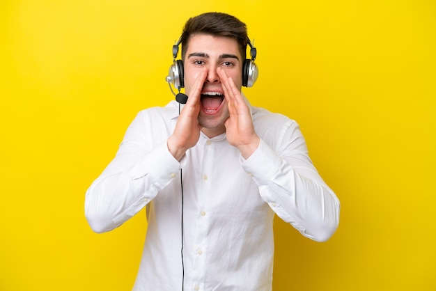 Télévendeur homme caucasien travaillant avec un casque isolé sur fond jaune criant et annonçant quelque chose