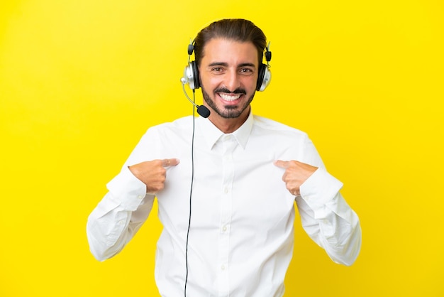 Télévendeur homme caucasien travaillant avec un casque isolé sur fond jaune avec une expression faciale surprise