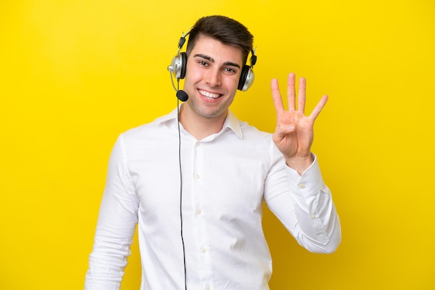 Télévendeur homme caucasien travaillant avec un casque isolé sur fond jaune heureux et comptant quatre avec les doigts