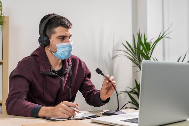 Télévendeur ou homme podcast travaillant avec un ordinateur portable et parlant sur un casque avec masque facial au bureau