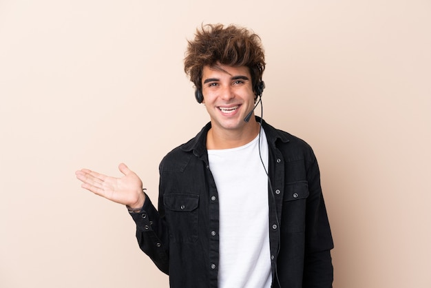 Télévendeur homme travaillant avec un casque sur un mur isolé tenant copyspace imaginaire sur la paume