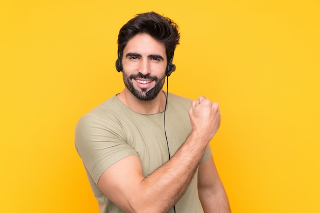 Télévendeur homme travaillant avec un casque sur un mur jaune isolé célébrant une victoire