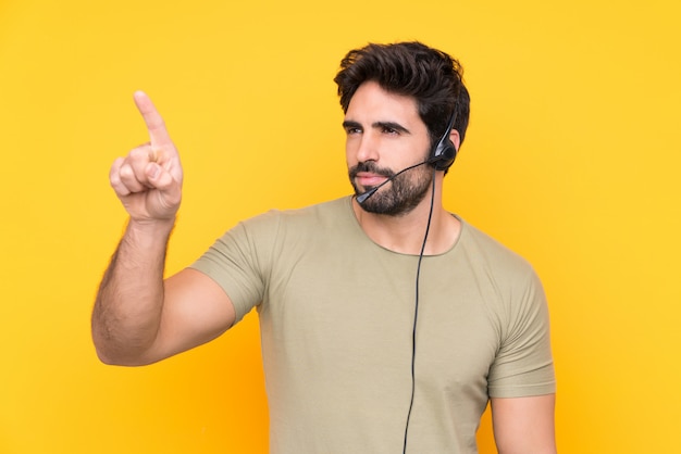 Télévendeur homme travaillant avec un casque sur un mur jaune isolé touchant sur un écran transparent