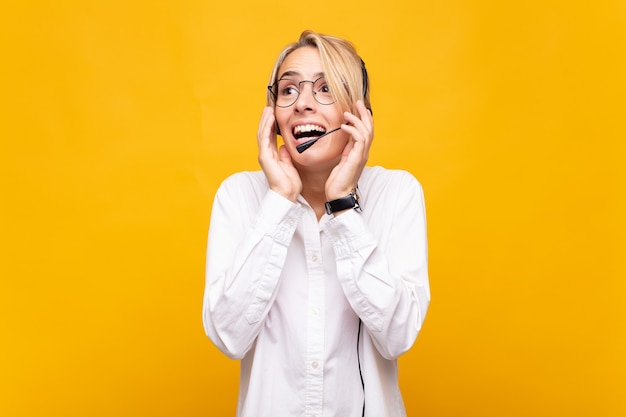 Télévendeur jeune femme se sentir heureux, excité et surpris, regardant sur le côté avec les deux mains sur le visage