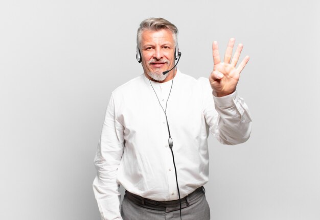 Télévendeur senior souriant et semblant amical, montrant le numéro quatre ou quatrième avec la main vers l'avant, compte à rebours