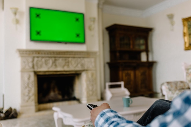 Photo télévision à écran vert vierge avec main féminine défocalisée tenant la télécommande