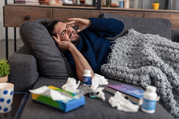 Une telle douleur. Malheureux jeune homme allongé sur le canapé alors qu'il souffre d'une forte migraine