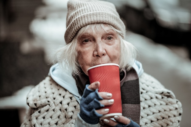 Tellement chaud. Triste pauvre femme debout avec une tasse de thé en le buvant