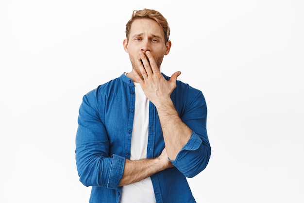 Tellement ennuyeux Un jeune homme rousse indifférent bâillant et ayant l'air fatigué ou indifférent à la caméra en regardant quelque chose d'inintéressant mourir d'ennui fond blanc