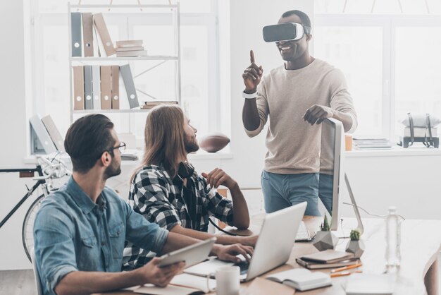 Tellement vrai! Équipe de développement coopérant dans leur bureau tandis que le beau jeune homme ajustant le casque VR et souriant