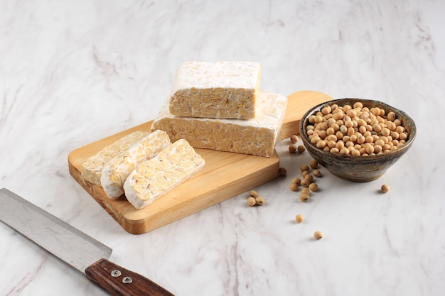 Tempeh cru ou Tempe. Tranches de tempeh sur fond de bois, coupées par une femme chef asiatique. Tempe à base de soja fermenté. Copier l'espace pour le texte