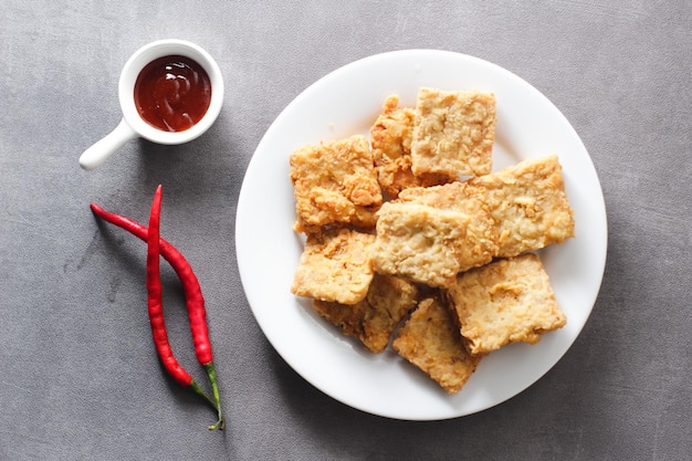 Tempeh frit croustillant sur une plaque blanche avec un fond gris