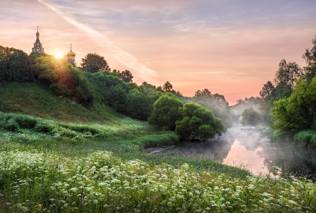 Temple sur un ciel rose d'aube sur un rivage brumeux de la rivière à Buzharovo