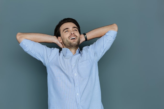 Temps agréable. Heureux homme positif joyeux mettant les mains sous la tête et souriant tout en profitant de son repos