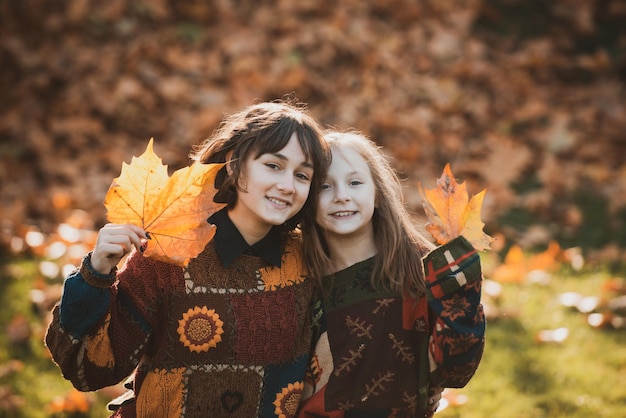 Temps chaud et ensoleillé jeune femme et fille avec des feuilles d'automne à la main et fond d'érable jaune d'automne