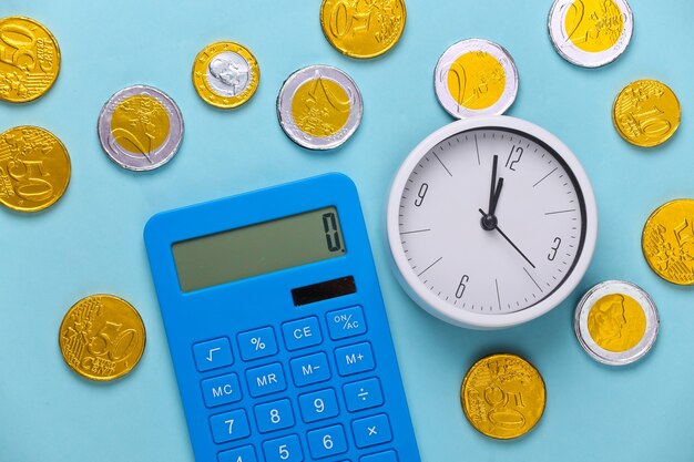 Le temps, c'est de l'argent. Horloge blanche avec calculatrice et pièces de monnaie sur bleu