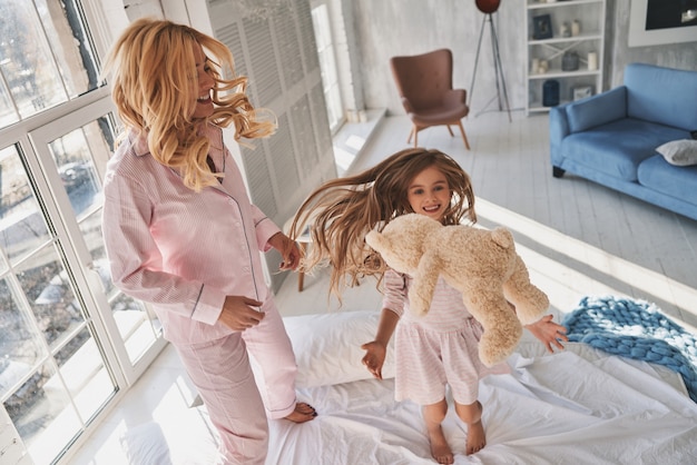 Temps libre ensemble. Vue de dessus d'une jolie petite fille sautant sur le lit avec sa mère tout en passant du temps à la maison