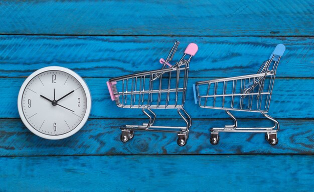 Temps de magasinage. Chariots de supermarché avec horloge sur une surface en bois bleue. Minimalisme. Vue de dessus