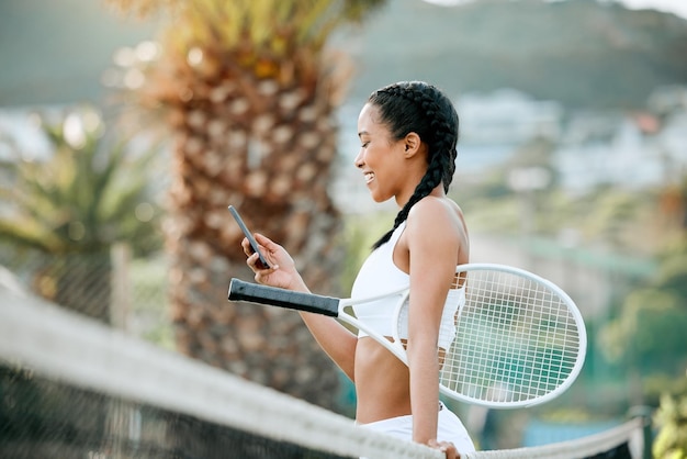 Le temps de pause est pour les connexions rapides. Photo d'une jeune femme sportive utilisant un téléphone portable tout en jouant au tennis sur un court.