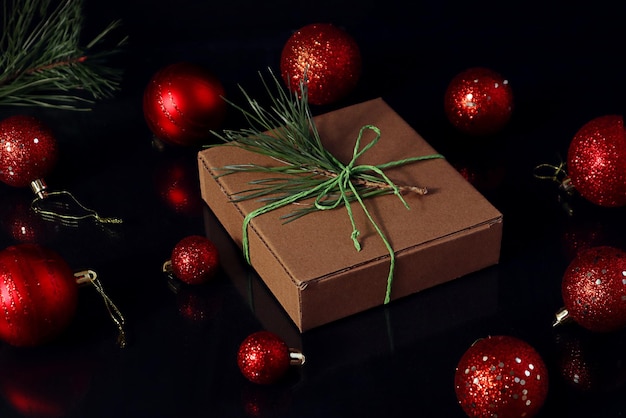 Temps pour les cadeaux du Nouvel An émouvants un cadeau emballé avec une branche de pin sur un fond sombre à côté de boules de Noël rouges